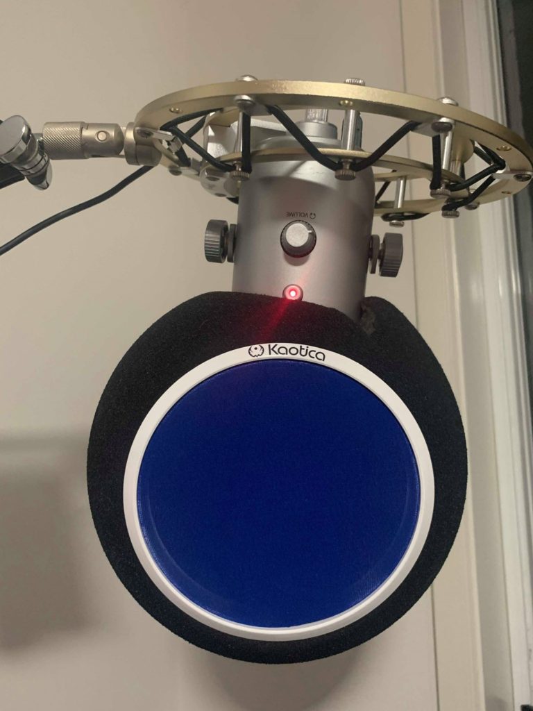 A silver blue yeti brand mic hanging from a boom arm with a black foam eyeball and blue pop filter